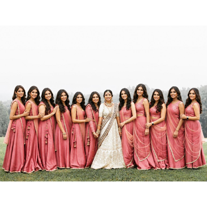 Group of women in pink sarees with one in a white saree, standing on grass.